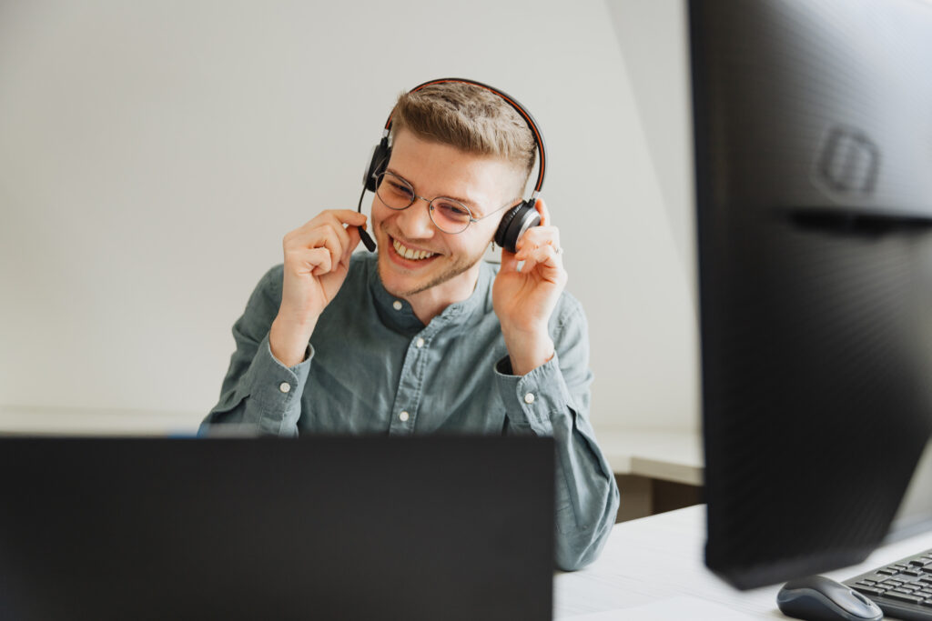 Mitarbeiter von TODAY Experts lächelt und führt mit Headset ein Gespräch an seinem Arbeitsplatz