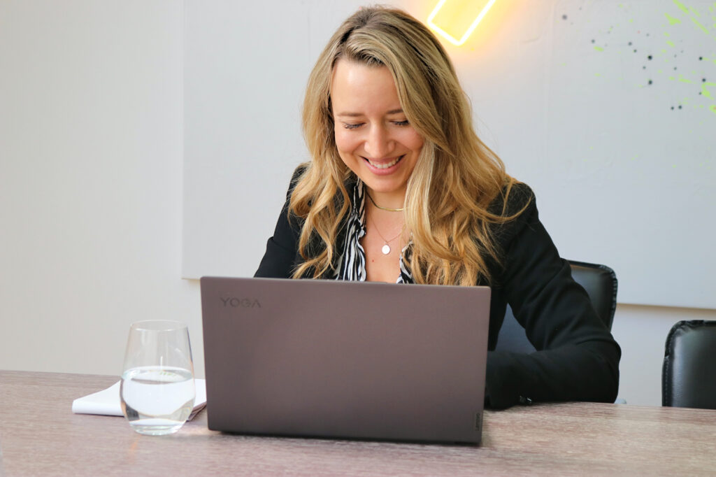 Zufriedene Kundin arbeitet lächelnd am Laptop an ihrem Arbeitsplatz