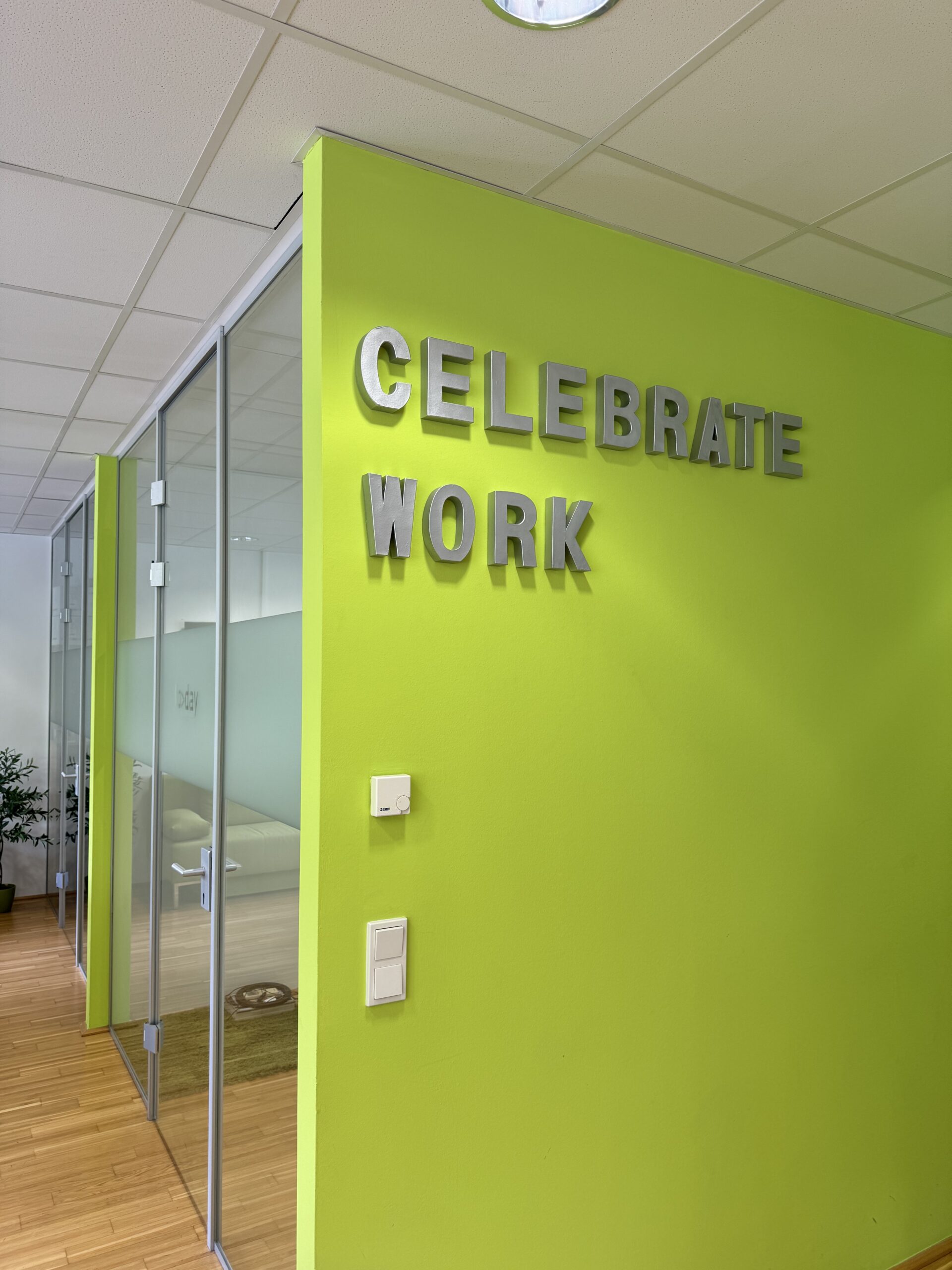 Besprechungsraum im Büro von TODAY Experts mit dem Wand-Schriftzug ‚Celebrate Work‘.“