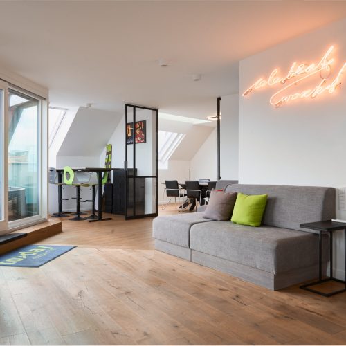 Modernes Büro bei TODAY Experts mit Couch, Sitzgelegenheiten und neonfarbenem ‚Celebrate Work‘-Schriftzug an der Wand
